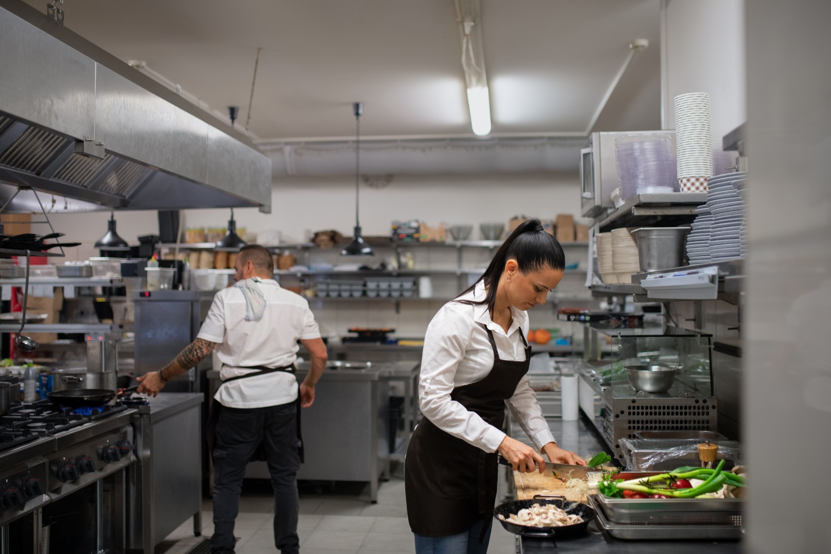 A professional female chef cutting vegetables indoors in restaurant kitchen.